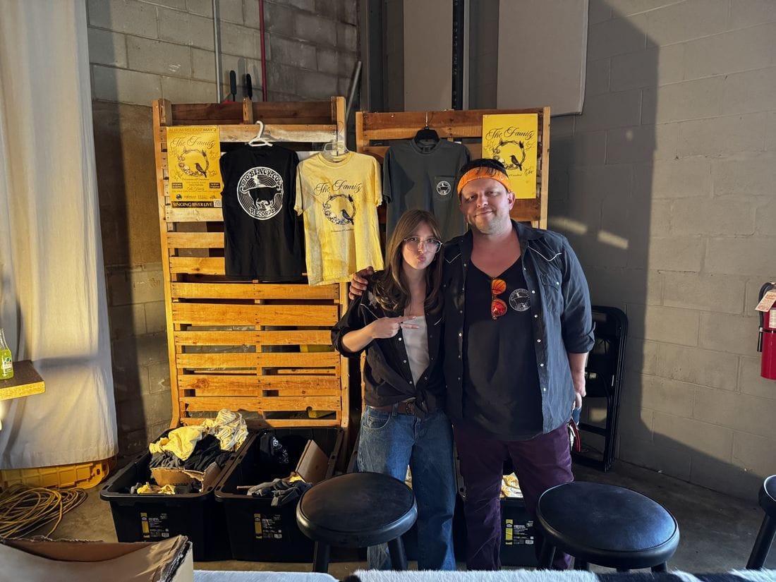 Jesse and Scarlett at a BBCR merchandise display with Family shirts and posters.